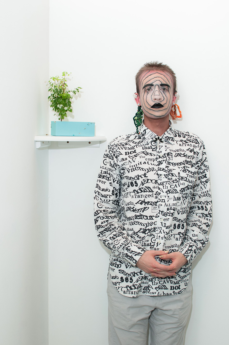 Jesse standing facing the camera with concentric circles drawn on his face wearing a patterned shirt against a white wall